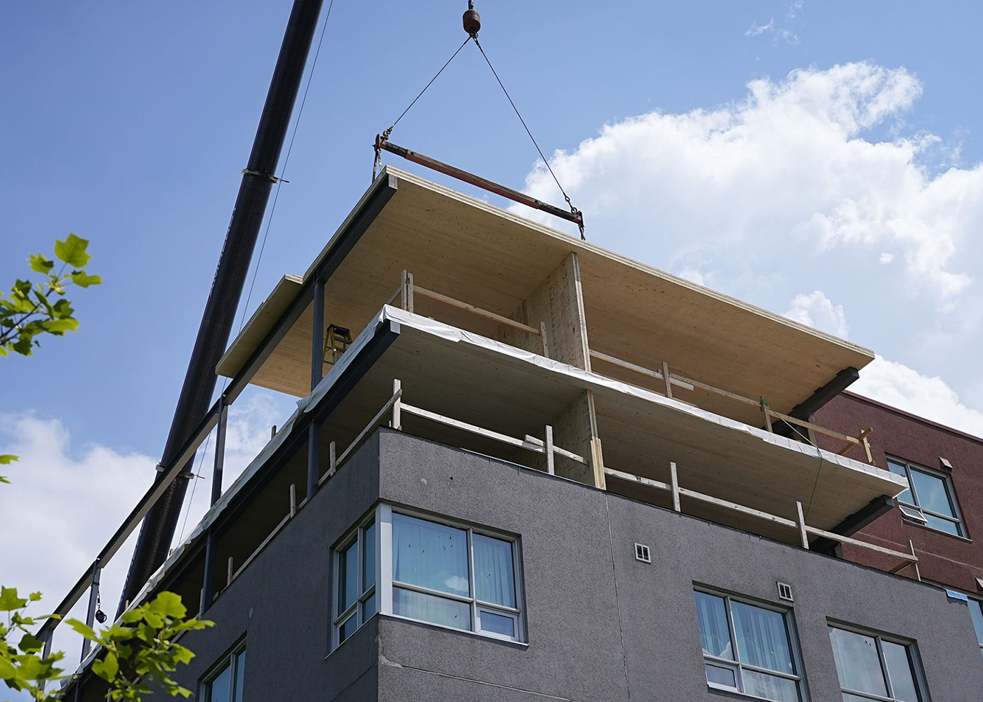 Crane lifting a mass timber panel above the existing roofline